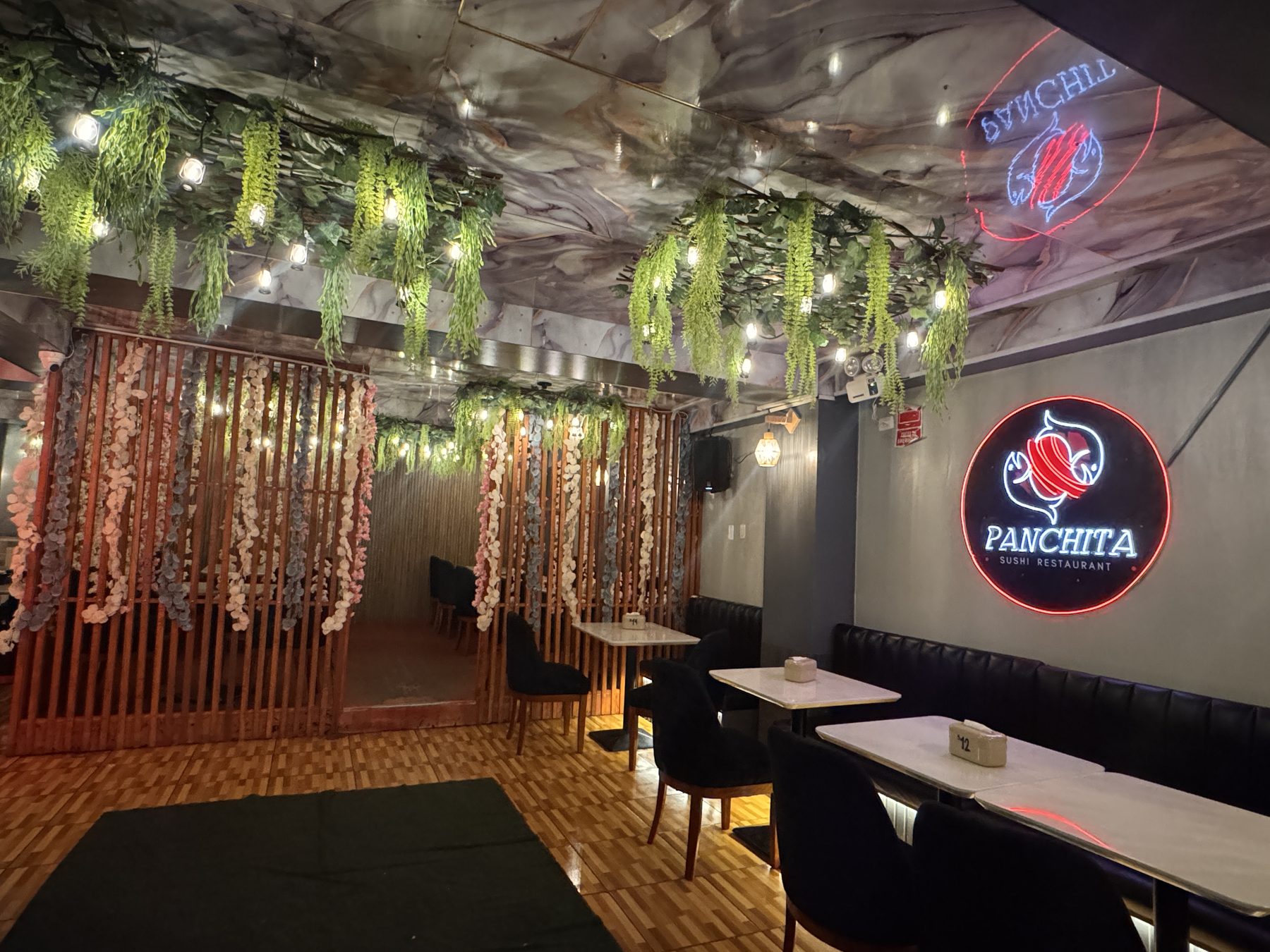 Salón de Panchita Sushi Restaurant en Cerro de Pasco, con techo de mármol, plantas colgantes y su logo de neón en la pared